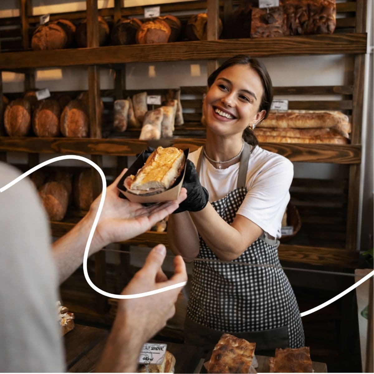 A smiling member of staff hands a sandwich to a guest across the counter.